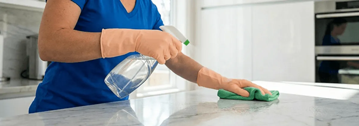 Maid service worker spraying and wiping a kitchen countertop with a microfiber cloth for sanitizing, Arvada, CO.